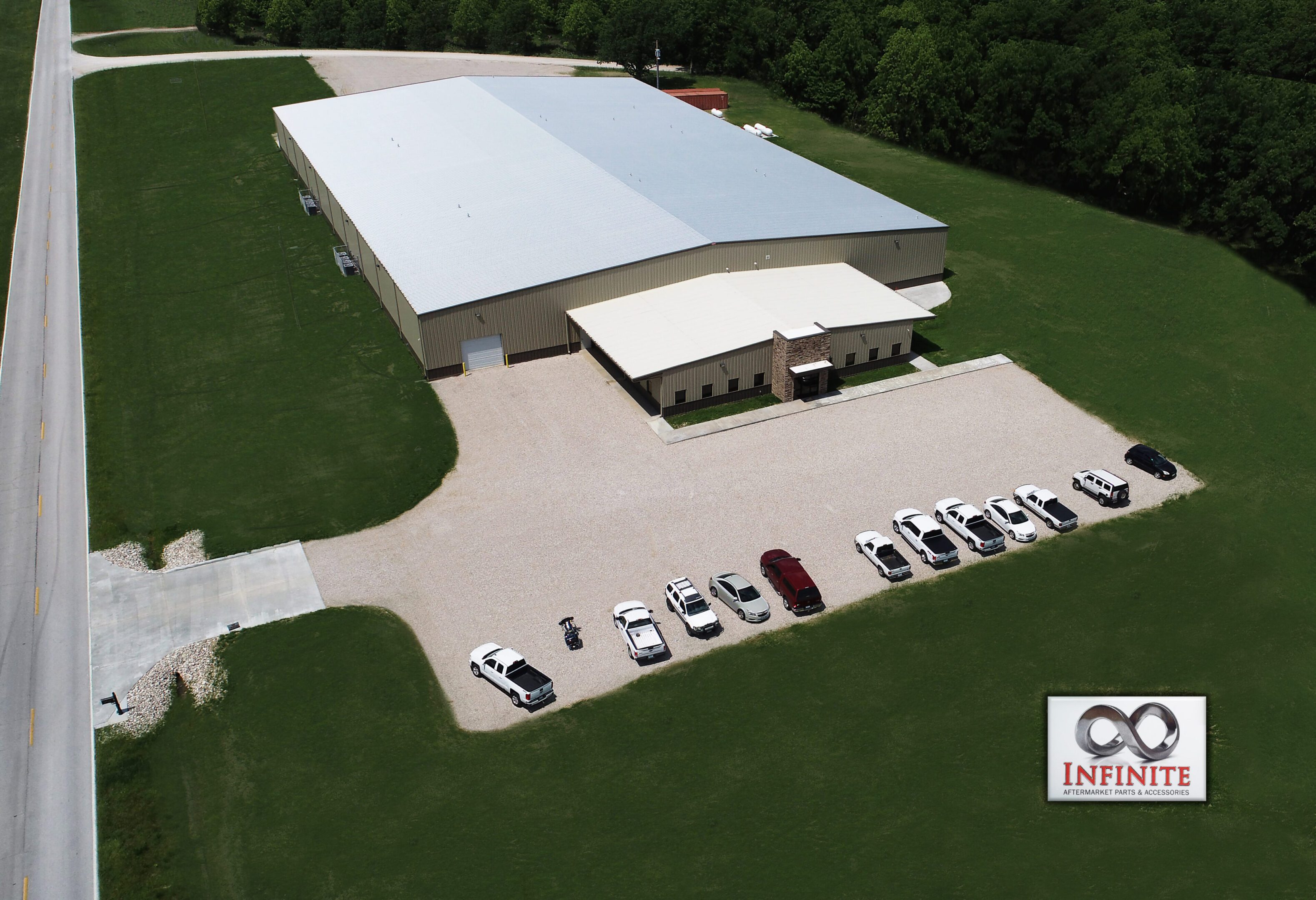 Aerial view of a large industrial building with parking lot and vehicles.