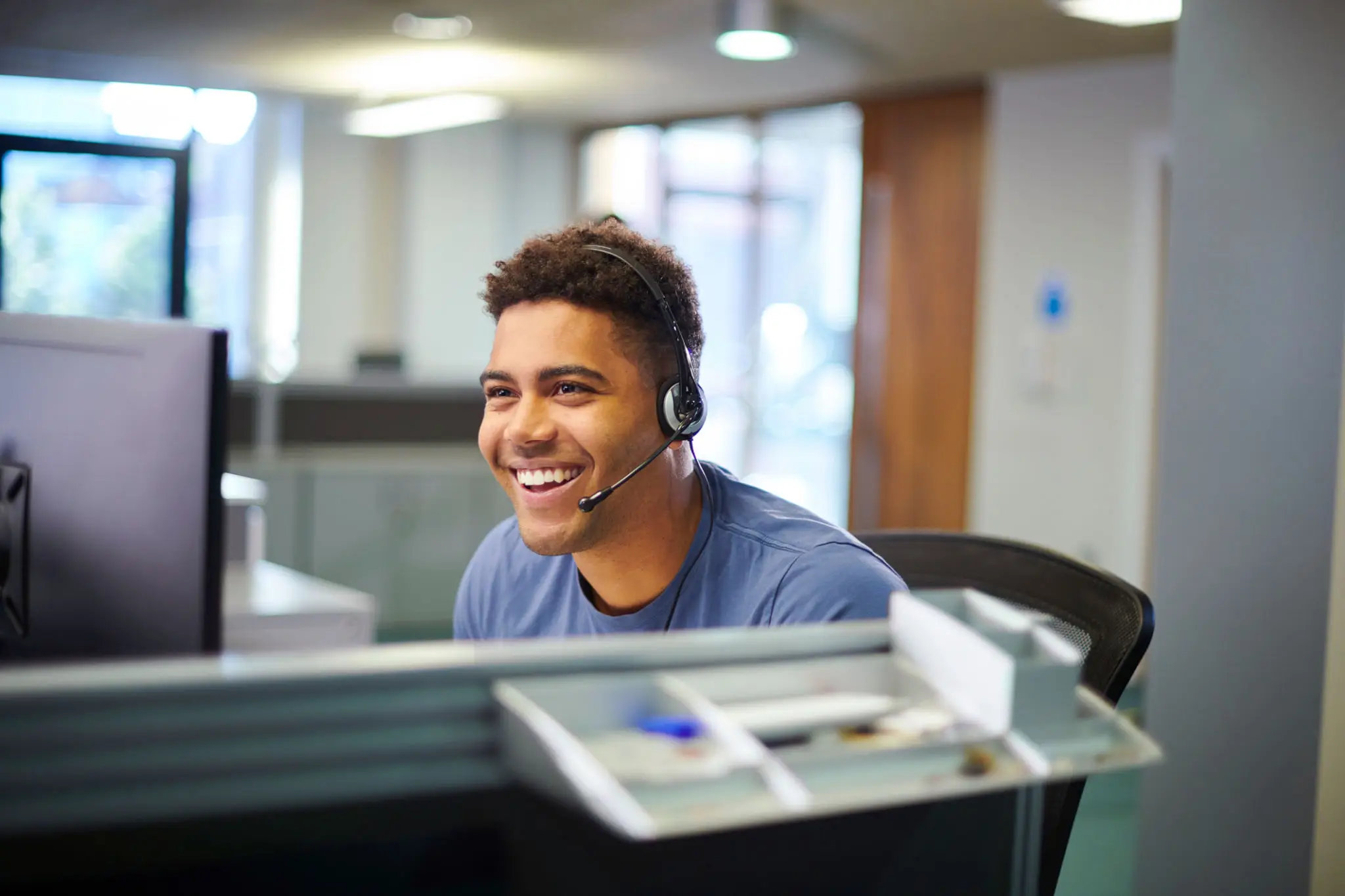 Smiling man wearing a headset working at a computer in an office.