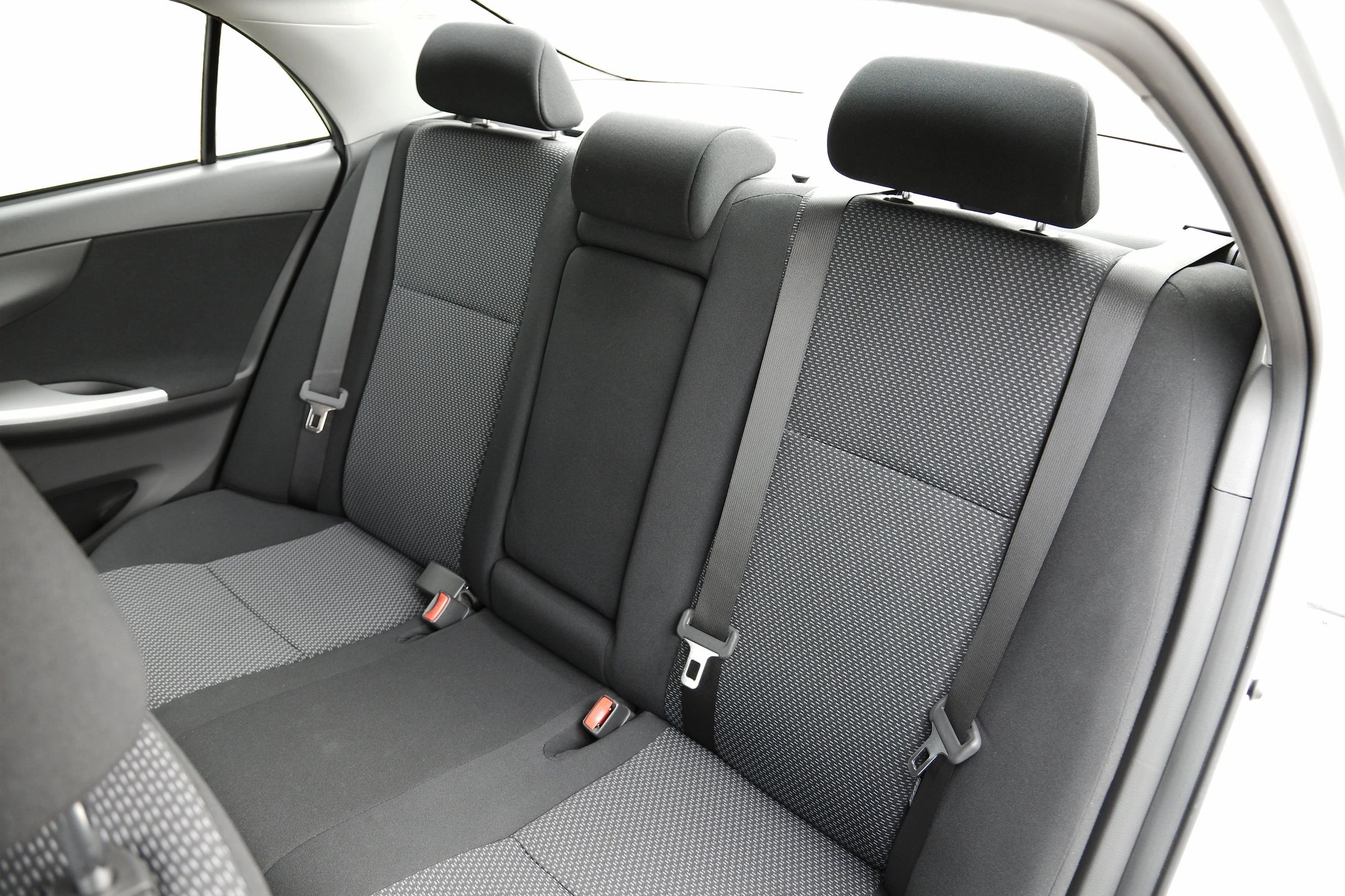 Clean black fabric car backseat with headrests and seatbelts.