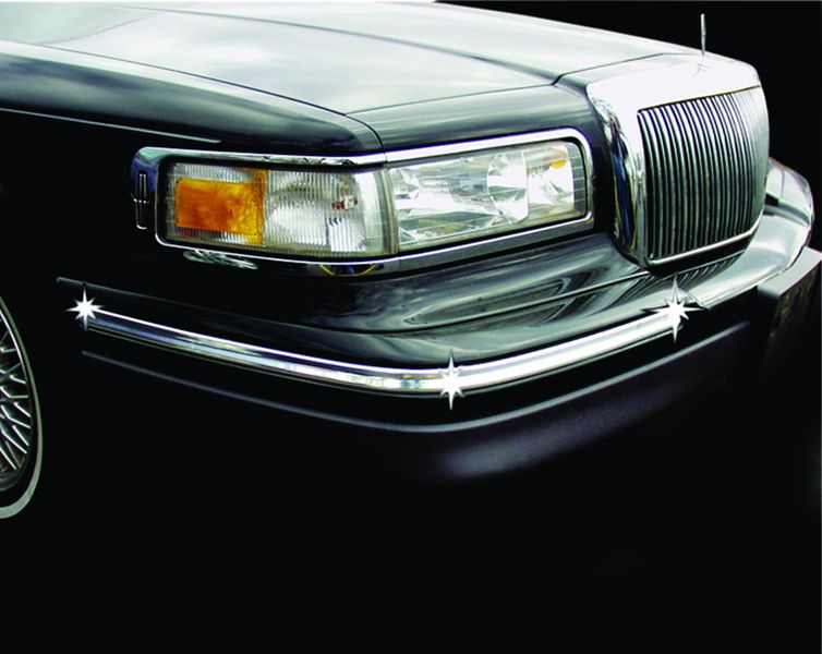 Close-up of a classic black car's front headlight and grille with shiny chrome detailing.